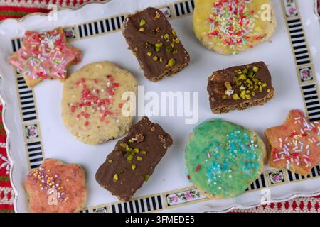 Petits biscuits au beurre avec des pépites colorées et des biscuits au chocolat et aux pistaches, arrangés pour Noël sur des assiettes de service, nappe de Noël Banque D'Images