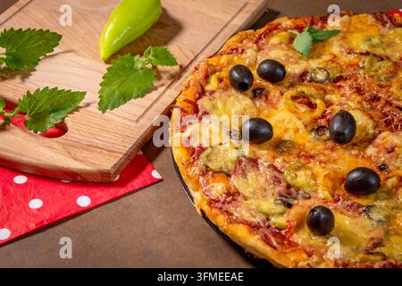 Pizza maison avec poivrons, olives, mozzarella sur une planche en bois. Forme ronde, pâte épaisse, petites tranches de poivron, fines tranches d'olive, feuilles de menthe Banque D'Images