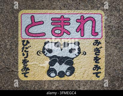 Shizuoka, Atami – 26 mars 2025 : Panneau de sécurité routière japonais arborant une illustration de panda sur le trottoir, incitant les enfants à regarder à gauche et Banque D'Images