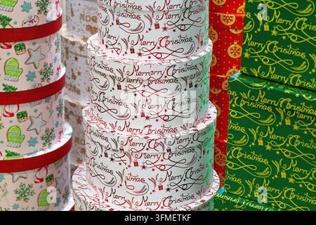 Close-up de boîtes-cadeaux de Noël empilées rondes et carrées enveloppées dans des motifs festifs colorés avec texte «Joyeux Noël», adaptées pour les emballages de fêtes Banque D'Images