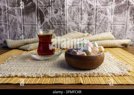 Nature morte turque traditionnelle mettant en scène un verre de thé noir et un bol en bois de délicatesse turque colorée (lokum). Servie sur un tissu tissé et du bambou Banque D'Images