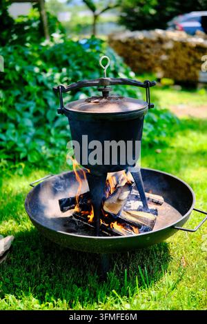Chaudière traditionnelle en fonte Dutch oven cuisant des aliments sur des flammes de bois de feu dans le foyer de jardin. Banque D'Images