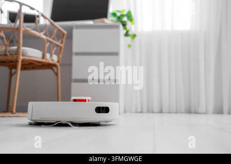 Automatisation de la maison intelligente et nettoyage domestique, aspirateur robotique travaillant sur le sol dans un salon moderne avec des meubles et une lumière vive par la fenêtre Banque D'Images