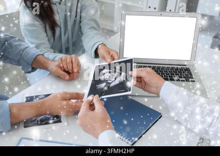 Soins prénataux et consultation de grossesse, médecin expliquant une échographie aux futurs parents dans un cabinet médical avec ordinateur portable et dossiers médicaux Banque D'Images