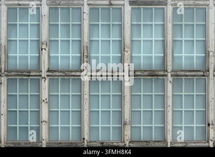 Des rangées de vieilles fenêtres en bois avec du verre bleu pâle et des panneaux quadrillés créent une façade symétrique et patinée arborant de la peinture blanche écaillée et une texture Banque D'Images