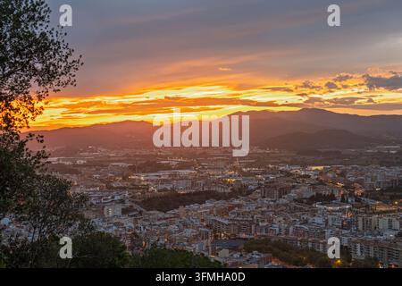 Une vue panoramique étendue d'une ville résidentielle en Espagne à un coucher de soleil doré vibrant, avec des montagnes ondulantes et des nuages dramatiques superposés à travers le soir Banque D'Images