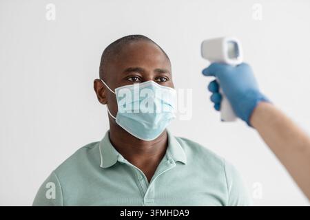 Soins de santé des patients, préparation pour la vaccination de la population et vérification de la personne avant la procédure. Médecin portant un masque de protection mesure la température avec Banque D'Images