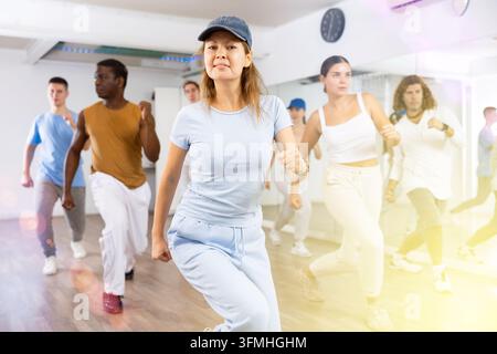 Classe de jeunes danseurs actifs adultes effectuant des marches pendant l'exercice de danse moderne ensemble dans la salle de danse Banque D'Images