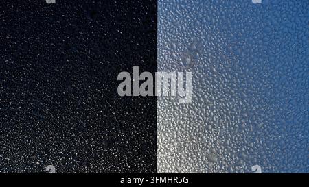 Des gouttelettes d'eau s'accrochent à une surface en verre. L'image divisée contraste un ciel nocturne sombre avec du verre réfléchissant. De minuscules perles captent la lumière sur une surface lisse. Perfec Banque D'Images