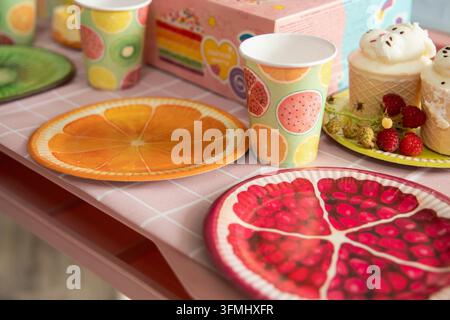 Table de fête d'anniversaire sur le thème des fruits colorés avec des gobelets en carton, des assiettes, des cupcakes et des framboises Banque D'Images
