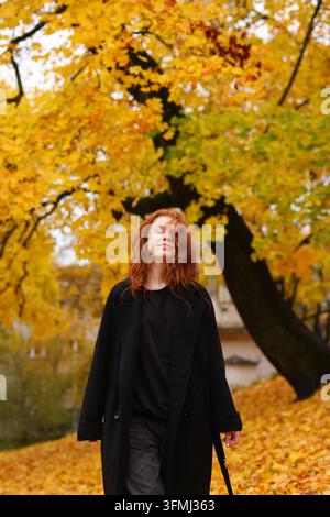 Jeune femme pensive posant parmi un feuillage doré, représentant la pleine conscience, la beauté naturelle et les moments paisibles de l'automne. Banque D'Images