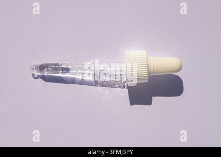 Goutteur de sérum transparent sur fond violet pastel pour concept de produits de soins et de beauté Banque D'Images