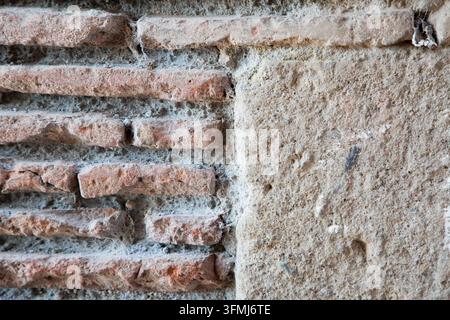 Mur de briques rouges patiné avec du mortier rugueux et une surface de plâtre vieillie, montrant une texture en gros plan, un détail de construction rustique, des tons terreux, la dégradation et Banque D'Images