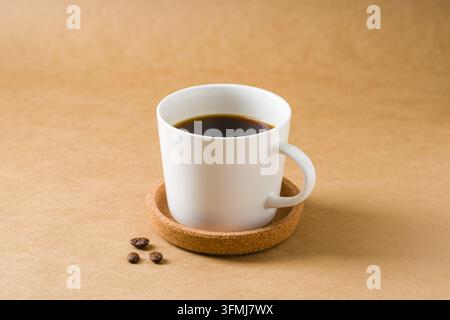 Tasse de café noire minimale avec des grains éparpillés sur une table chaude Banque D'Images