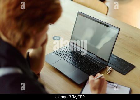Femme travaillant sur un ordinateur portable et prenant des notes au bureau Banque D'Images