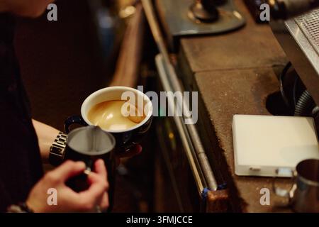 Barista versant du lait vaporisé dans une tasse pour créer des motifs de latte art dans un café Banque D'Images