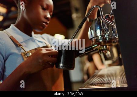 Barista noire fait mousser du lait avec une machine à expresso Banque D'Images
