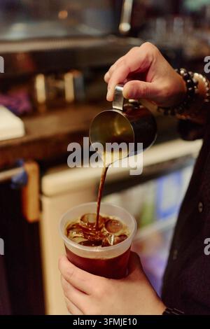 Mains de barista versant un espresso frais sur de la glace dans un café Banque D'Images