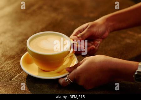 Femme tenant une tasse jaune de café latte frais avec art de table Banque D'Images