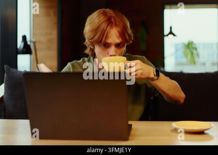 Homme buvant du café tout en travaillant sur un ordinateur portable dans un café Banque D'Images