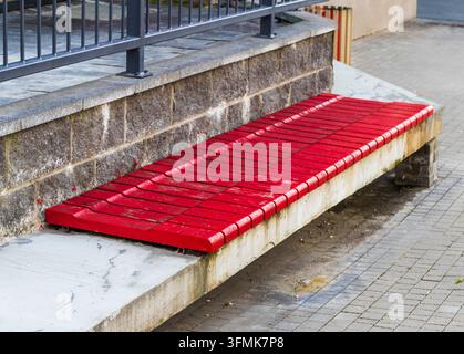 Banc long en bois moderne peint en rouge sur une base en béton et pierre Banque D'Images