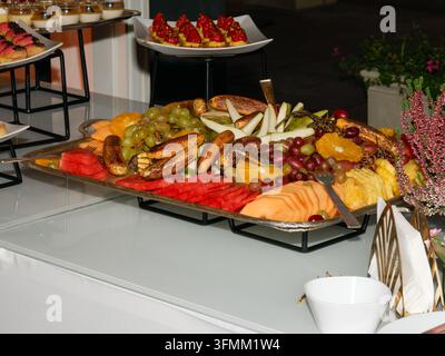 Assiette de fruits frais tranchés comprenant des raisins, de la pastèque, du melon et de l'ananas sur une table de buffet. Banque D'Images