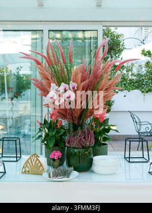 Arrangement floral décoratif avec des orchidées roses et des graminées dans des vases verts sur une table en plein air. Banque D'Images