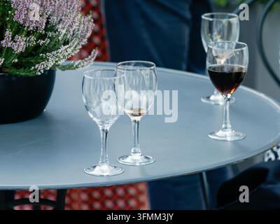 Verres à vin sur une table ronde grise de patio avec une plante de bruyère en pot à côté. Banque D'Images