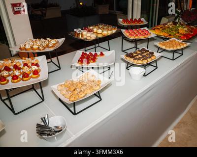 Variété de petits desserts et pâtisseries variés exposés sur des assiettes blanches et des supports sur une table. Banque D'Images