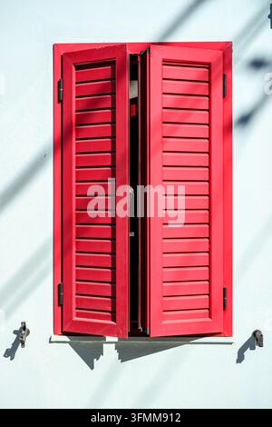 Volets rouges ouverts sur un mur blanc Banque D'Images