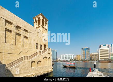 Bateau traditionnel en bois Abra naviguant le long du Dubai Creek devant l'architecture historique des tours à vent à Al Seef, Dubaï, Émirats Arabes Unis Banque D'Images