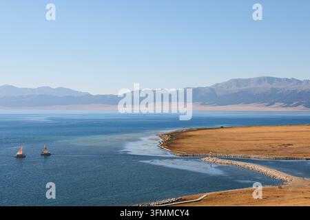 Vue automnale pittoresque des montagnes du lac Sayram au Xinjiang, en Chine, avec de minuscules voiliers sur le lac Banque D'Images