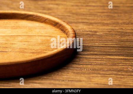 Vue plate en contre-plongée d’un dessous de verre rond en bois vide posé sur un fond en bois rustique avec un éclairage chaud et un large espace de copie à droite. Banque D'Images