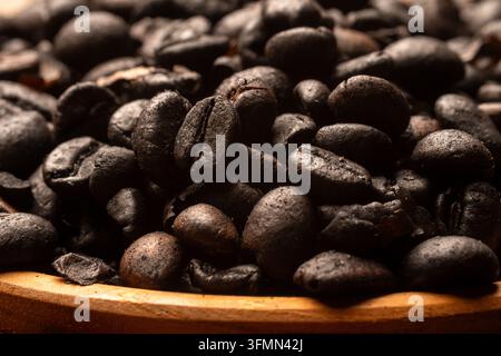 Prise de vue macro extrême en gros plan de la texture de surface de grains de café torréfiés sombres avec mise au point sélective et faible profondeur de champ pour fond de café. Banque D'Images
