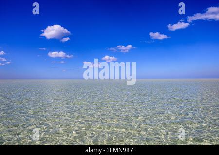 Beau ciel bleu ensoleillé avec des nuages duveteux sur une plage de mer turquoise claire Banque D'Images