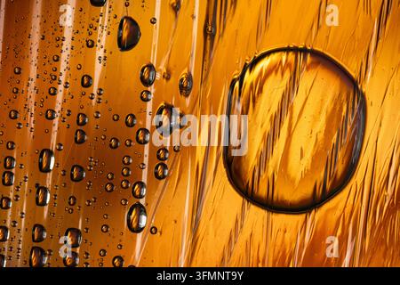 Les motifs de condensation prennent forme alors que des gouttelettes d'eau s'accrochent à une surface ambrée rugueuse, créant un fond liquide unique et artistique Banque D'Images