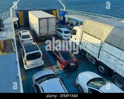 Vue aérienne de voitures et camions de marchandises arrimés sur le pont des véhicules d'une ferry traversant les eaux ouvertes, montrant le transport maritime, le transport routier de marchandises et les passagers Banque D'Images