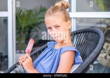Jeune Européenne blonde léchant une glace aux fruits rouges sur la terrasse d'été de la maison. Photo de haute qualité Banque D'Images