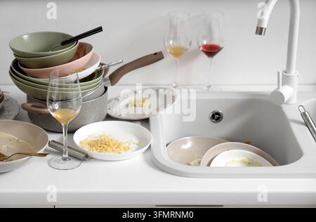 Ménages et épuisement domestique, pile de vaisselle sale et évier de cuisine en désordre après un dîner avec des restes de nourriture et des verres à vin Banque D'Images