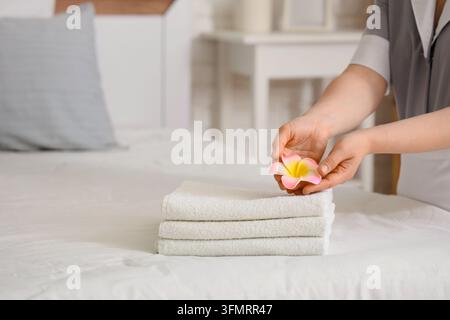 Hospitalité et service hôtelier, femme de chambre posant une fleur de plumeria sur des serviettes blanches fraîches dans la chambre d’hôte pour un hébergement de luxe et une expérience bien-être Banque D'Images