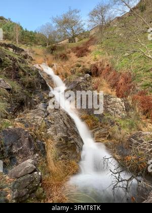 Une petite cascade dévale un terrain accidenté et rocheux à O Rosal, en Galice, en Espagne. Des hautes herbes et des arbustes épars sans feuilles bordent l'eau, tandis que s Banque D'Images