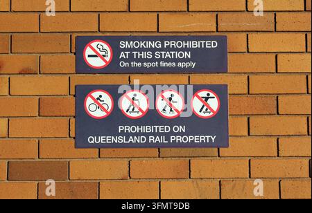 Panneaux de Queensland Rail montés sur un mur de briques brunes détaillant les interdictions de fumar, de vélo, de scooter et de skateboard Banque D'Images