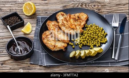 Veprovy rizek v testicku cuisine tchèque escalopes de porc sautées dans une pâte à l'œuf servies avec des petits pois, des tranches de concombre marinées dans une assiette, accompagnement de sauce sombre Banque D'Images