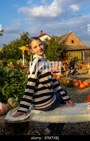 Jeune femme posant dans une ferme rustique de citrouilles en automne pendant l'heure dorée. Jeune femme posant parmi les citrouilles dans un cadre rustique d'automne pendant l'heure dorée. Banque D'Images