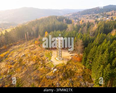 Vue aérienne de la tour d'observation Svetly vrch entourée d'une forêt de conifères dense avec un feuillage automnal et un terrain rocheux à Albrechtice v Jizerskych horách Banque D'Images