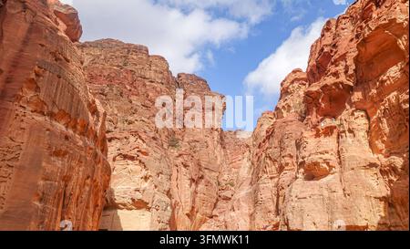 Vue de la gorge étroite du Siq avec des falaises de grès rouge imposantes sous un ciel bleu éclatant à Wadi Musa, gouvernorat de Ma'an, Jordanie. Banque D'Images