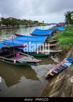 Bateaux fluviaux traditionnels en bois avec bâches bleues amarrés le long de la rivière Thu Bon à Hoi An Banque D'Images