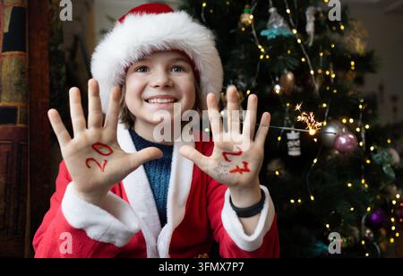 Paumes d'enfants avec les chiffres de la nouvelle année 2027 écrits dessus. Thème de Noël. Un garçon en costume du Père Noël. Espérances et espoirs pour une année lumineuse Banque D'Images