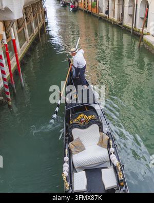 Venise, Italie - 21 septembre 2026 : Vue d'un gondolier ramant une gondole noire traditionnelle à travers un canal étroit, avec des bâtiments historiques et des rouges Banque D'Images