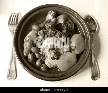 Vue aérienne d'une tagine de poulet marocaine avec citron confit, olives, pommes de terre et persil dans un restaurant traditionnel, photo sépia historique Banque D'Images